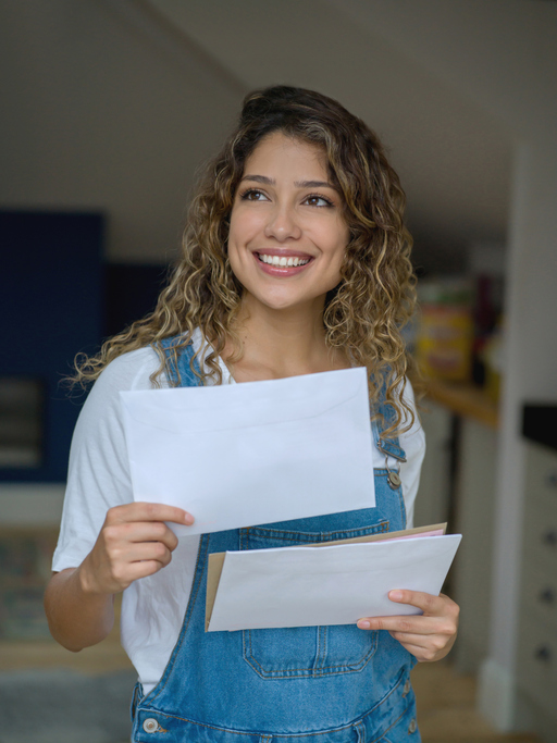 Beautiful young woman at home checking the mail looking up daydreaming very happy and smiling about her good grades