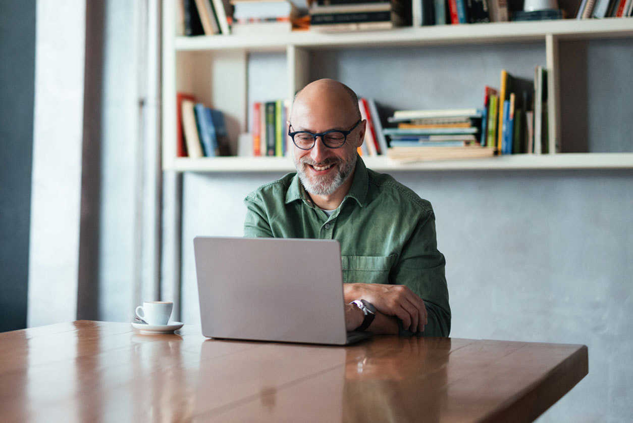 Smiling Man Working on Laptop in Modern Workspace with Bookshelves