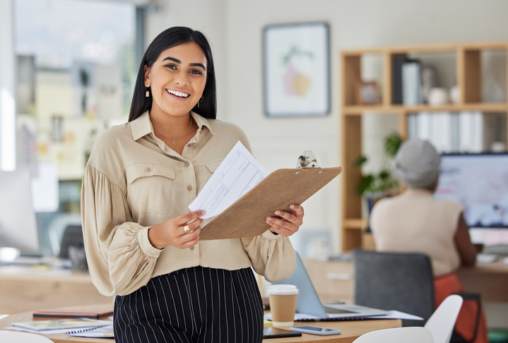 Review, contract and report with a business woman holding a clipboard with paperwork in her office at work. Application, document and proposal with a young female employee reading notes and working